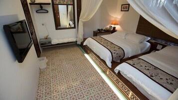 A hotel room with two beds, a mirror, a bedside table with a lamp, and a television.