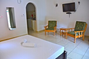 Una habitación de hotel con una cama, dos sillones tapizados en verde, un televisor y un espejo.
