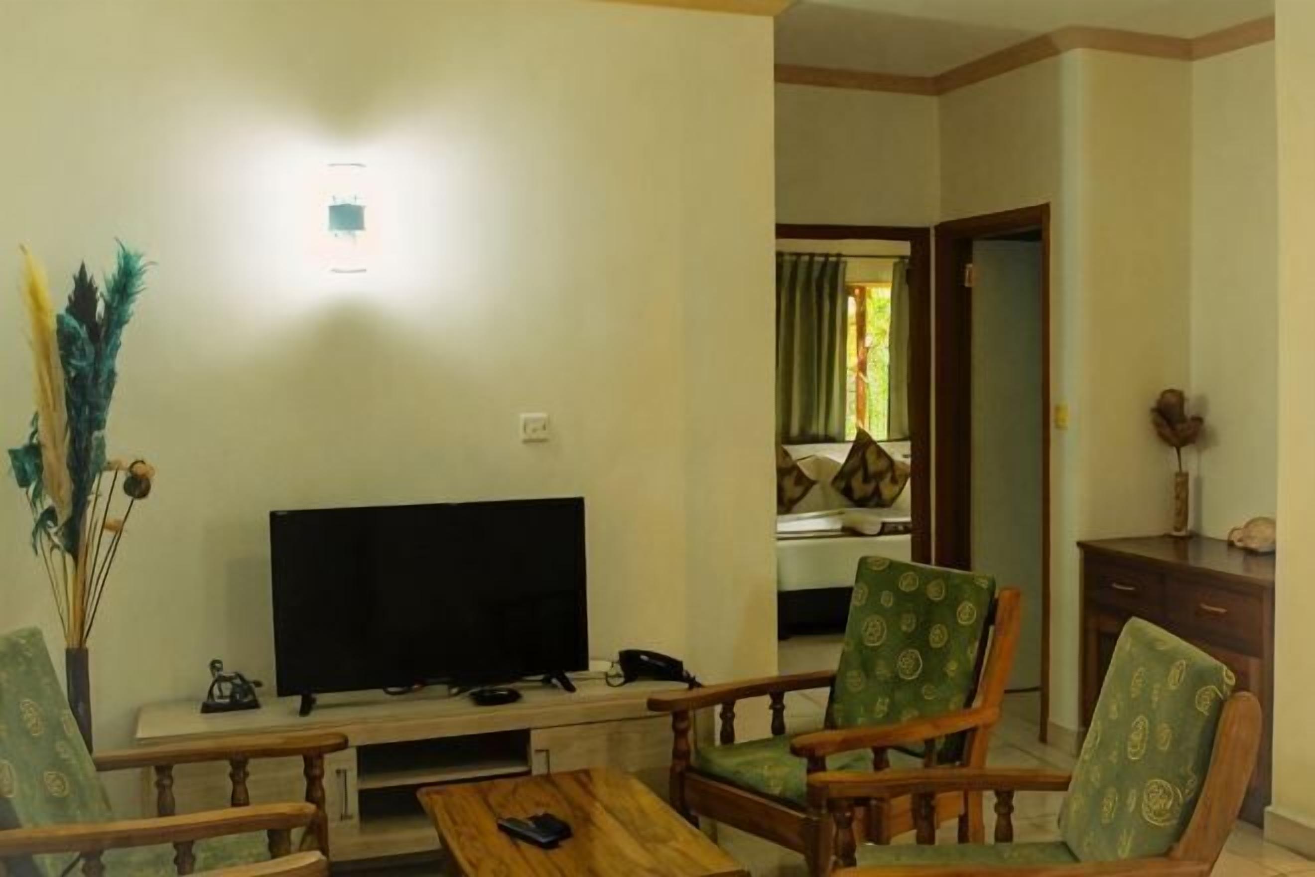 A living room with a flat-screen TV, wooden furniture, and a visible door leading to another room.