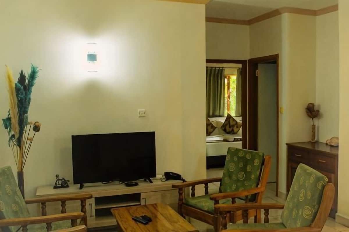 A living room with a flat-screen TV, wooden furniture, and a visible door leading to another room.