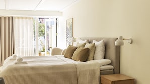 Une chambre à coucher avec un lit, une table de chevet, une lampe et une vue sur l’extérieur.