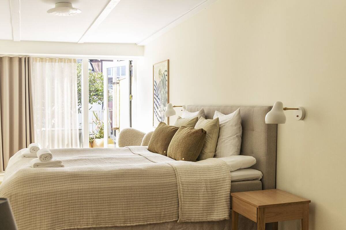 A bedroom with a bed, bedside table, lamp, and a view of the outdoors.