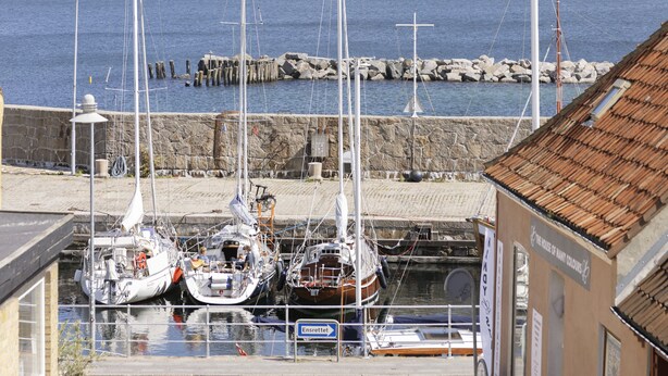 Un port où plusieurs voiliers sont amarrés, une jetée en pierre et un bâtiment sur lequel on peut voir une enseigne.