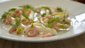 Une assiette de nourriture comprenant des crevettes, des herbes et, éventuellement, des pâtes ou des raviolis.