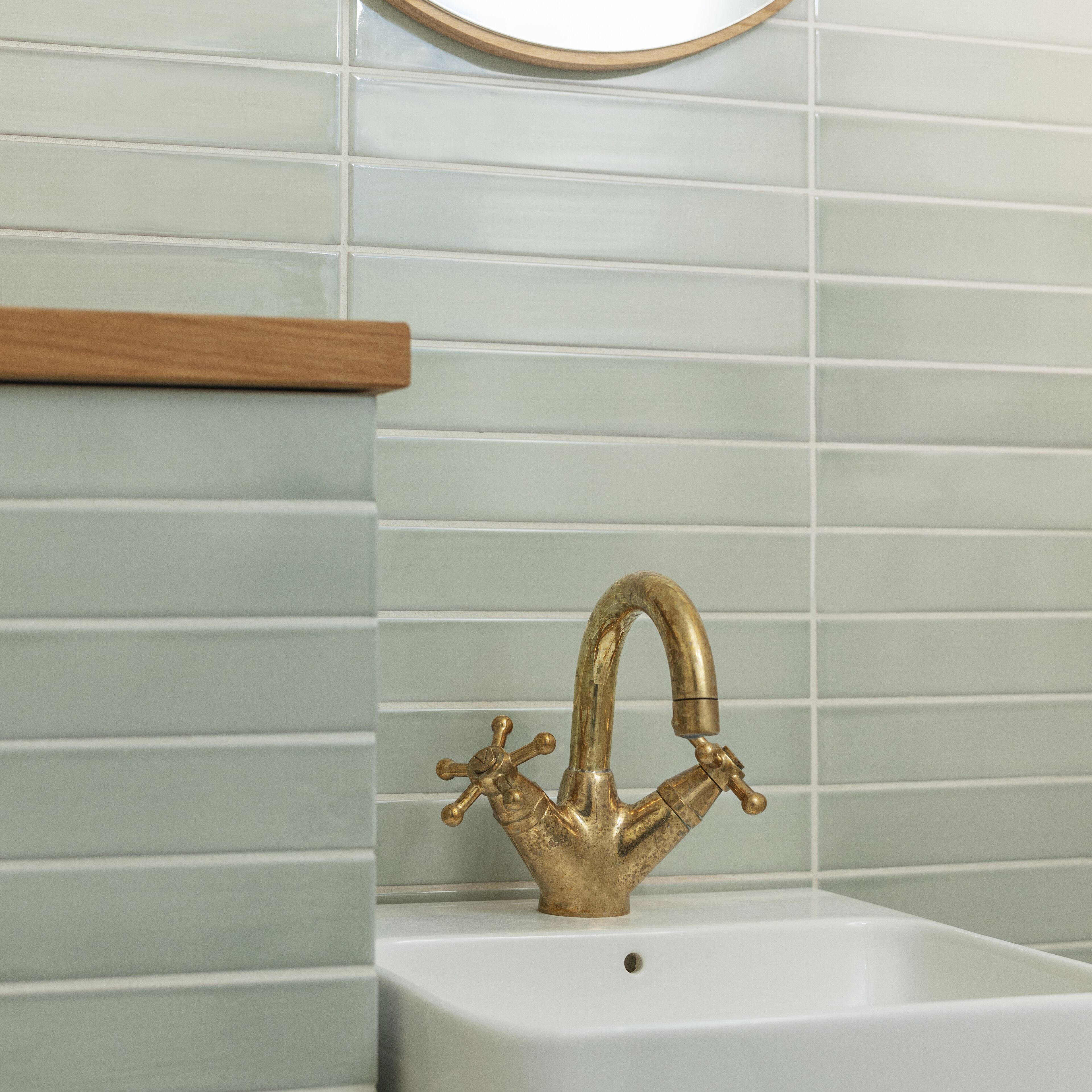 A bathroom with a white sink, a gold faucet, and light green tiled walls.