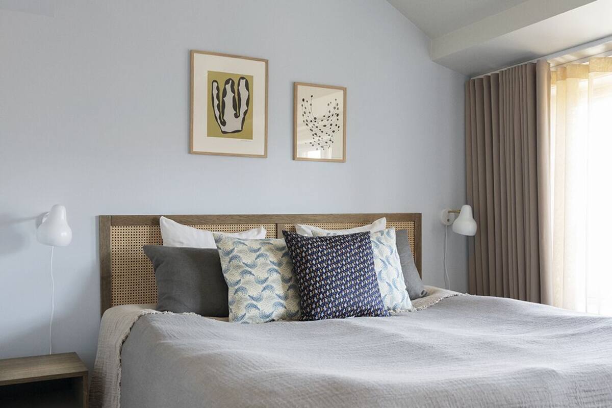 A bedroom with a large bed, two wall-mounted lamps, and two framed artworks.