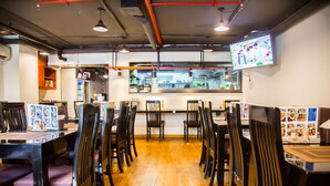Um restaurante com piso de madeira, cadeiras pretas e uma televisão fixada na parede.