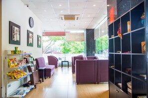 A modern interior with purple seating, a clock, and a view of greenery outside. - Sakura Hotel II (Hanoi)