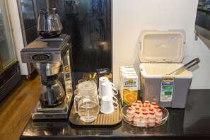 A coffee station with a coffee maker, cups, a pitcher, and a box of orange juice. - Sakura Hotel II (Hanoi)