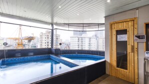 Piscina no terraço com vista para o horizonte urbano, sauna e porta de madeira.