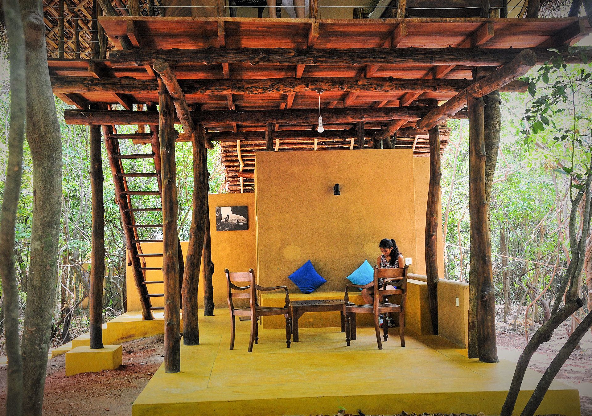 Une structure en bois comprenant un banc et des chaises, entourée d’arbres.