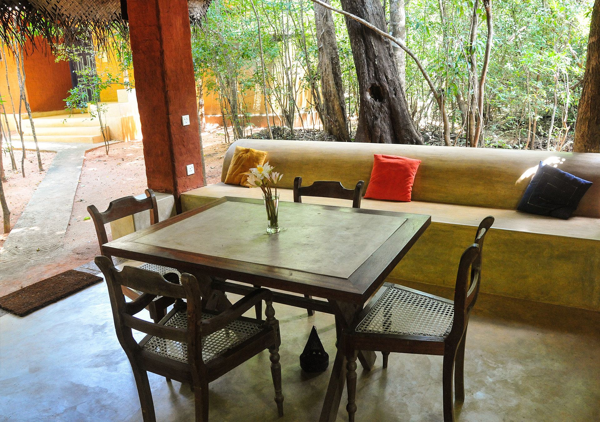 A wooden table with chairs and a bench in a shaded outdoor area with a view of trees.