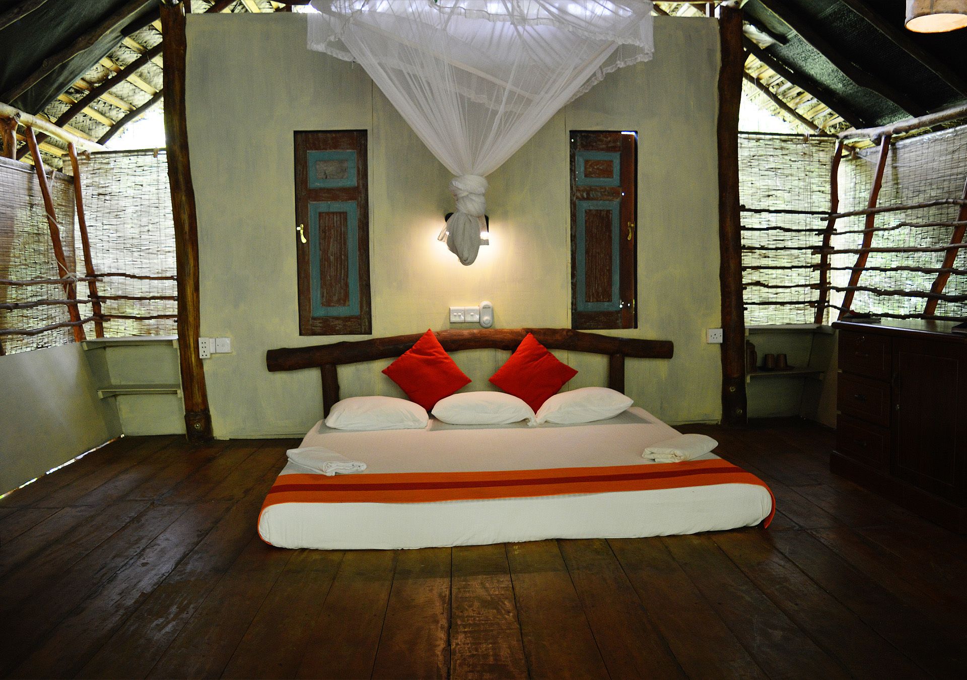 A room with a bed, wooden floor, and a mosquito net above the bed.
