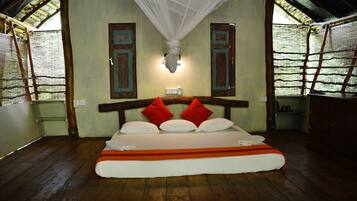 A room with a bed, wooden floor, and a mosquito net above the bed.