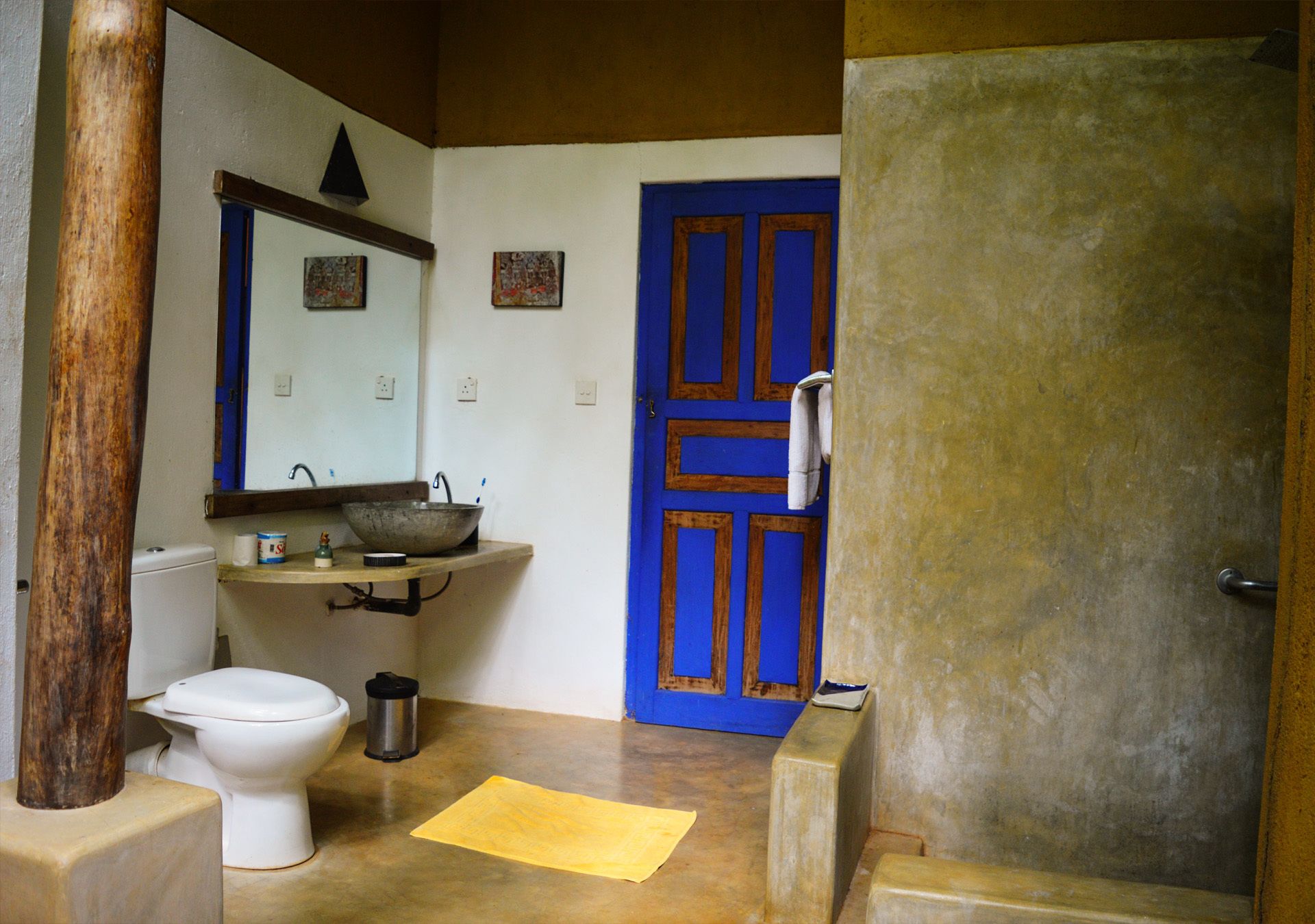 A bathroom with a white toilet, a sink with a large basin, a blue door, and a towel hanging on the door.