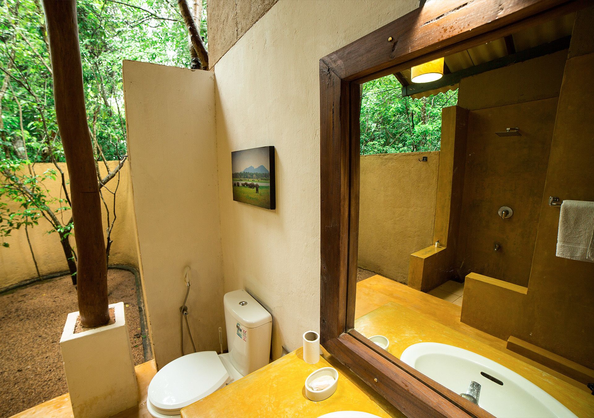 A bathroom with a wooden frame mirror, two sinks, a toilet, and a shower.