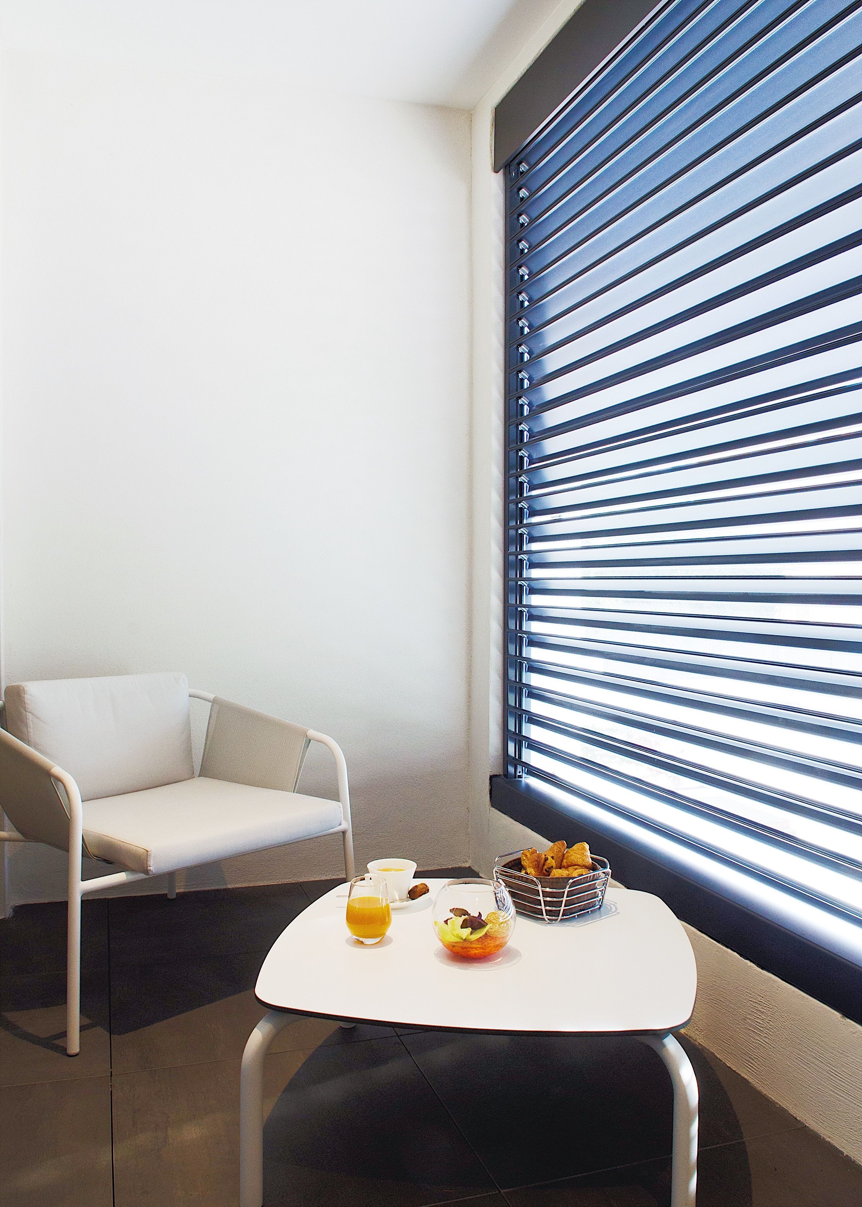 A modern room with a white sofa, a small table with breakfast items, and a window with horizontal blinds.