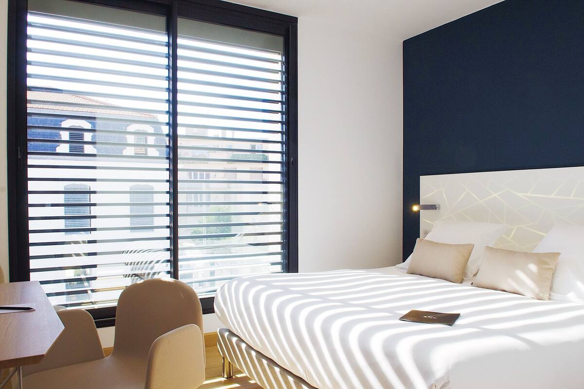 Quarto de hotel com cama, escrivaninha e cadeira.