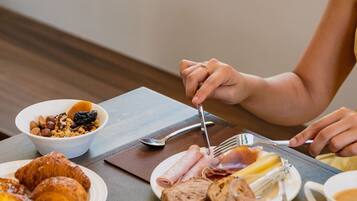 Une table en bois dressée pour le petit-déjeuner, avec des croissants, des fruits, du fromage et du jambon.