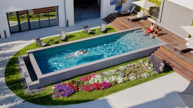 A modern outdoor swimming pool with a wooden deck, lounge chairs, and a flower garden. - Hôtel In Situ (Béziers)