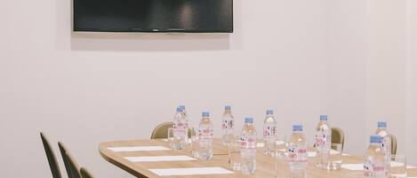 A conference room with a long table, chairs, a flat-screen TV, and water bottles.