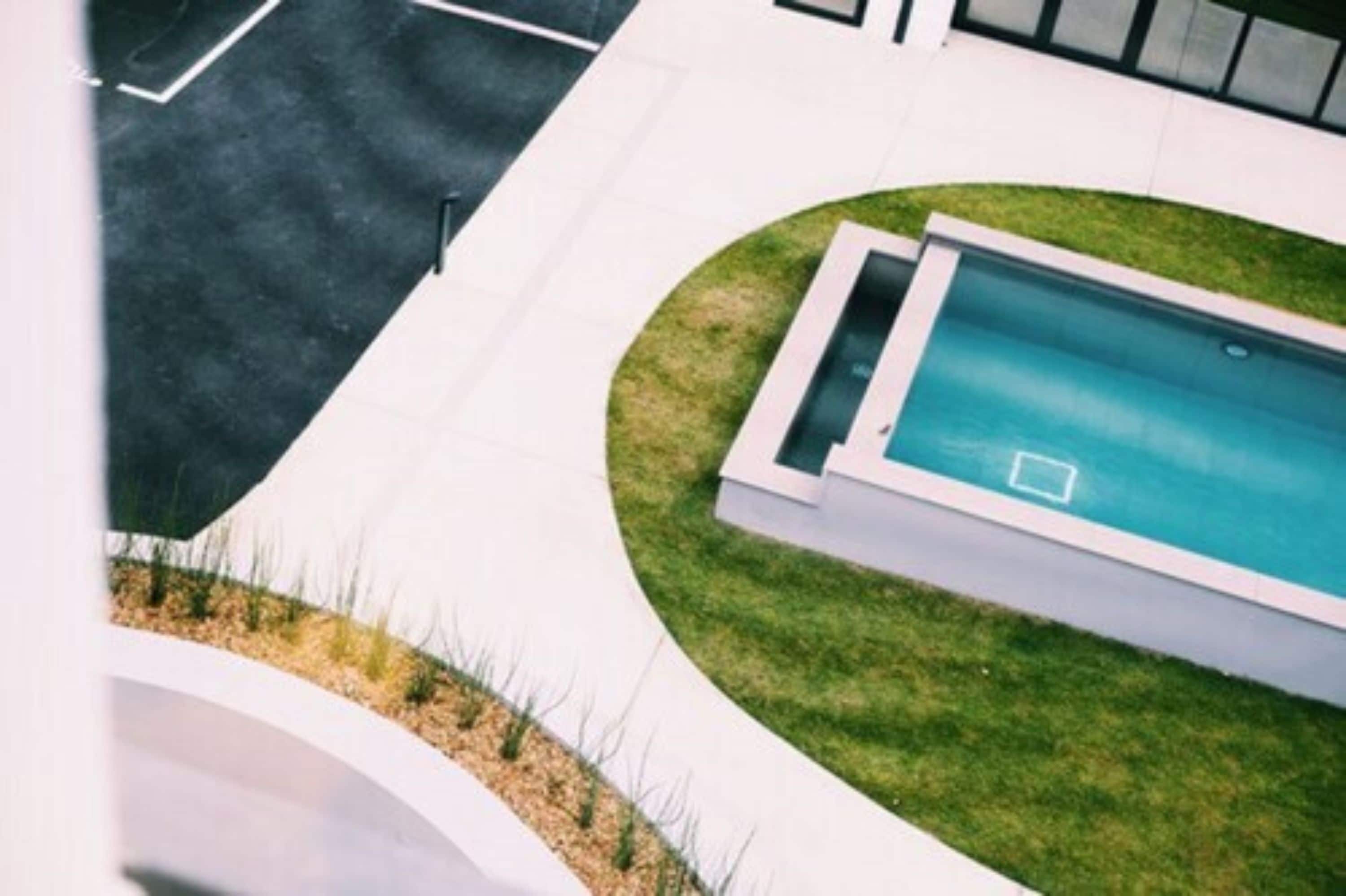 A modern swimming pool with a rectangular shape, surrounded by a well-maintained lawn and a curved white pathway.