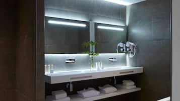 Een moderne badkamer met een grote spiegel, twee wastafels, een wastafelmeubel, een badkuip en een plank met handdoeken.