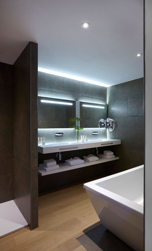A modern bathroom with a large mirror, two sinks, a vanity, a bathtub, and a shelf with towels.