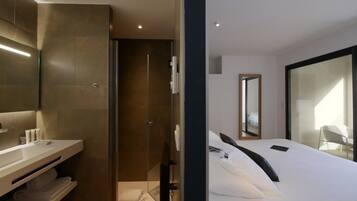 Une chambre d’hôtel moderne dotée d’un grand lit, d’une douche intégrée, d’une coiffeuse avec un miroir et d’une grande fenêtre.
