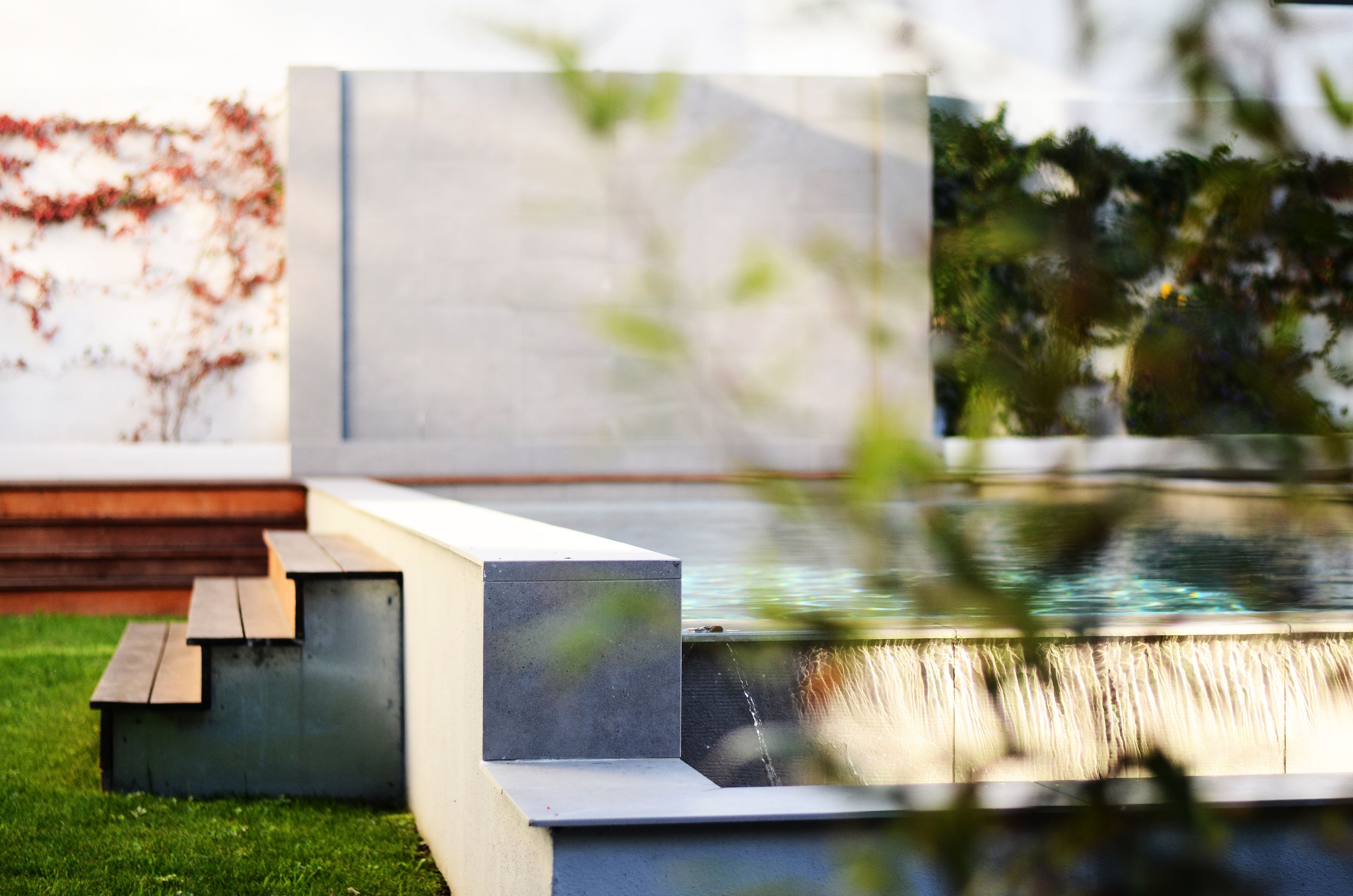 A modern outdoor area with a concrete structure, a small water feature, and a grassy area.