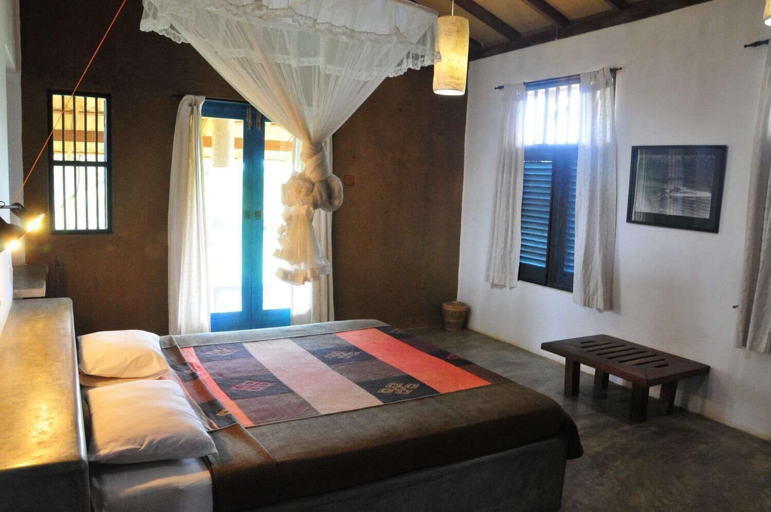 A room with a bed, a bench, a hanging light fixture, and a window with curtains.
