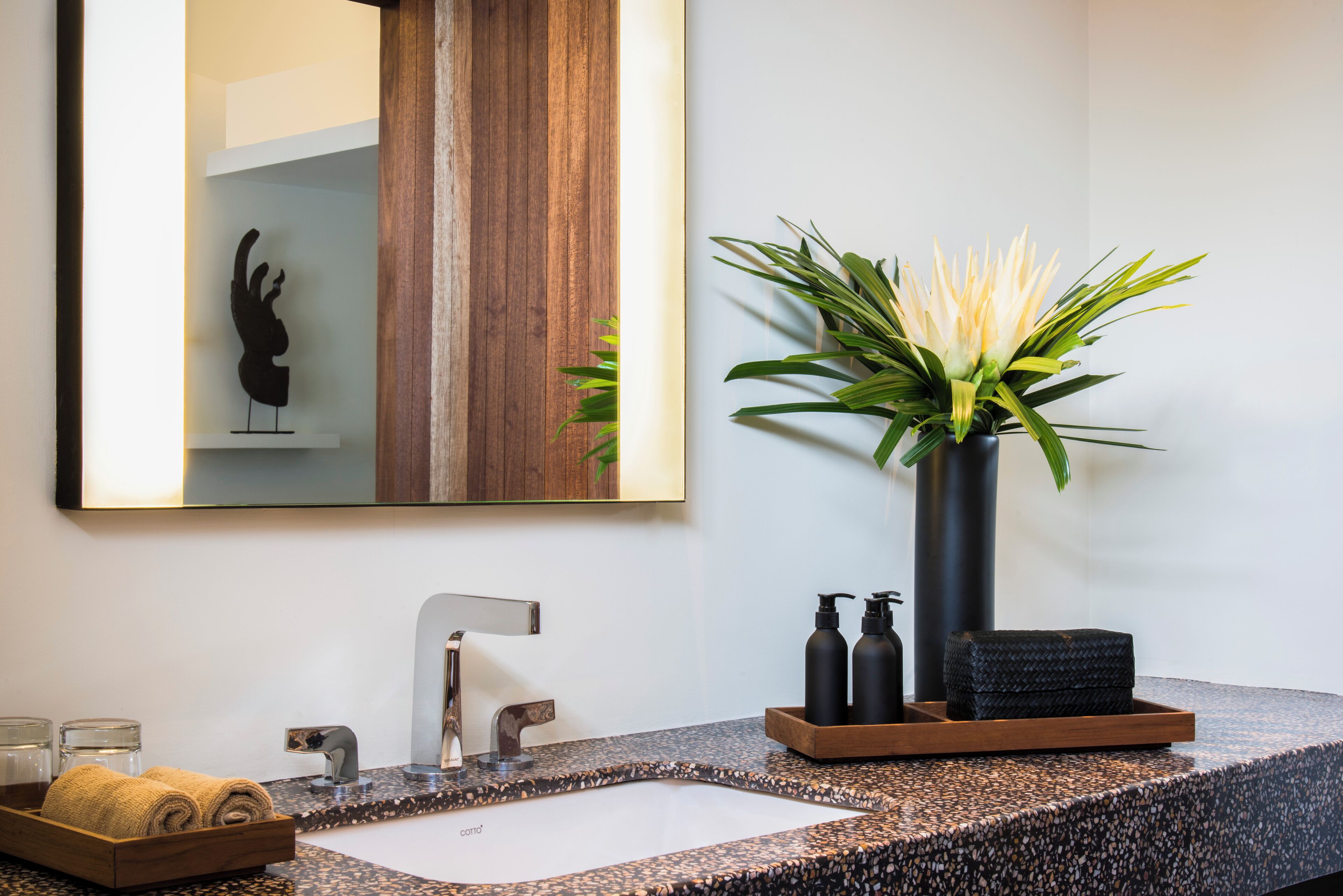 Un baño moderno con encimera de granito, un espejo grande, una planta en maceta y artículos de aseo.