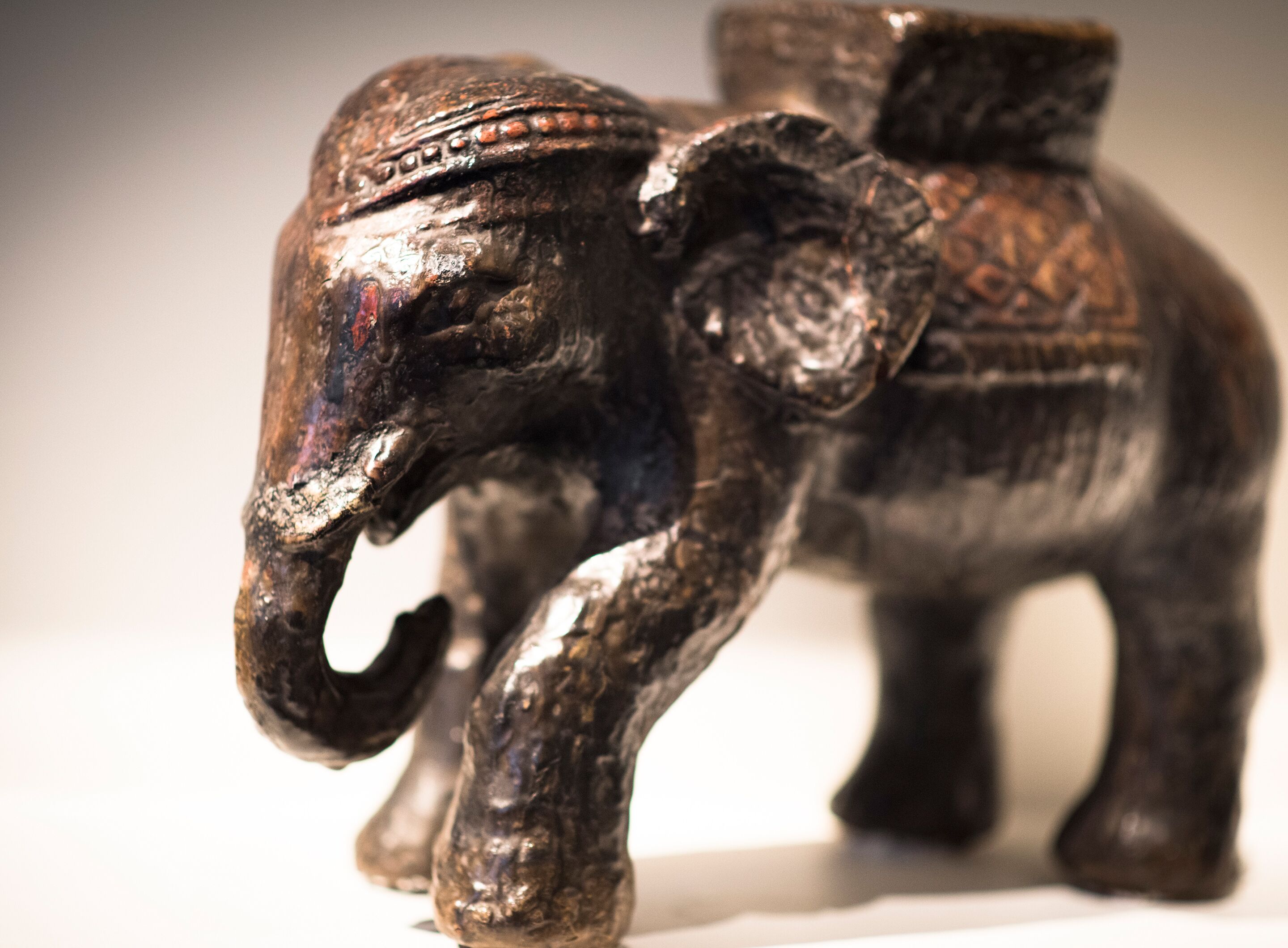Una pequeña escultura de madera oscura de un elefante, con tallas intrincadas y una pieza decorativa en la cabeza.