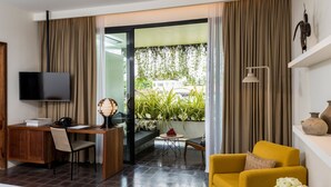 Une chambre d’hôtel équipée d’un bureau, d’une chaise, d’une télévision, d’un fauteuil jaune et offrant une vue sur la verdure environnante.
