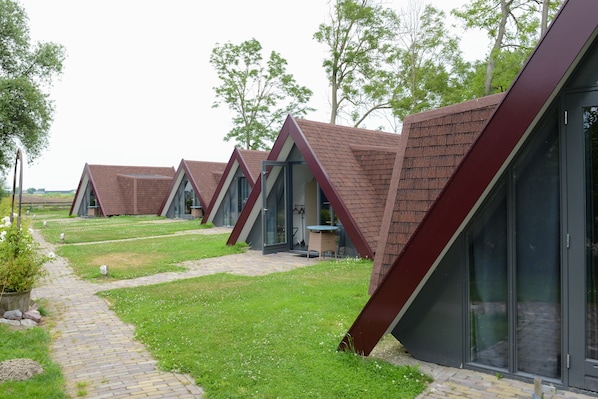 A row of modern, triangular-roofed buildings with glass windows, set in a grassy area with a paved walkway.