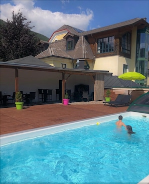 A pool area with a covered patio, a house with a sloped roof, and a mountain in the background.