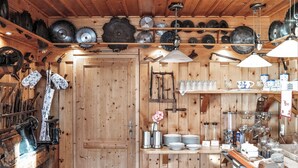 A rustic kitchen with wooden walls, shelves with tools, and a variety of kitchenware.