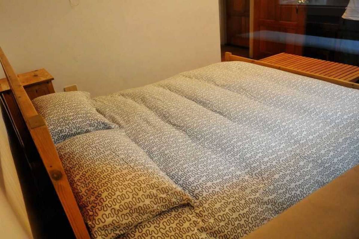 Una cama con colcha y almohadas estampadas, cabecera de madera y un banco de madera al pie de la cama.
