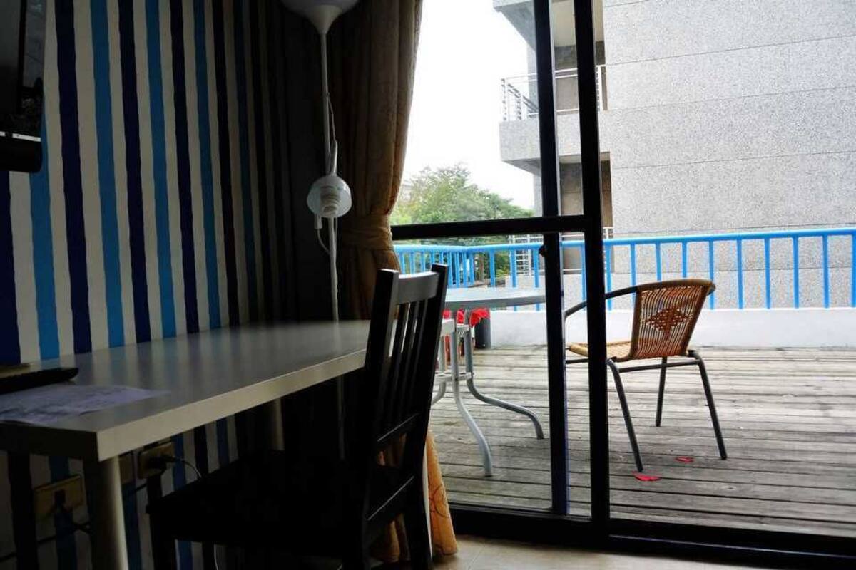 Una habitación con pared a rayas, una mesa, una silla y vistas a un balcón con barandilla.