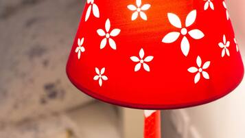 Luminária com cúpula vermelha estampada com motivos florais brancos, sobre superfície branca.