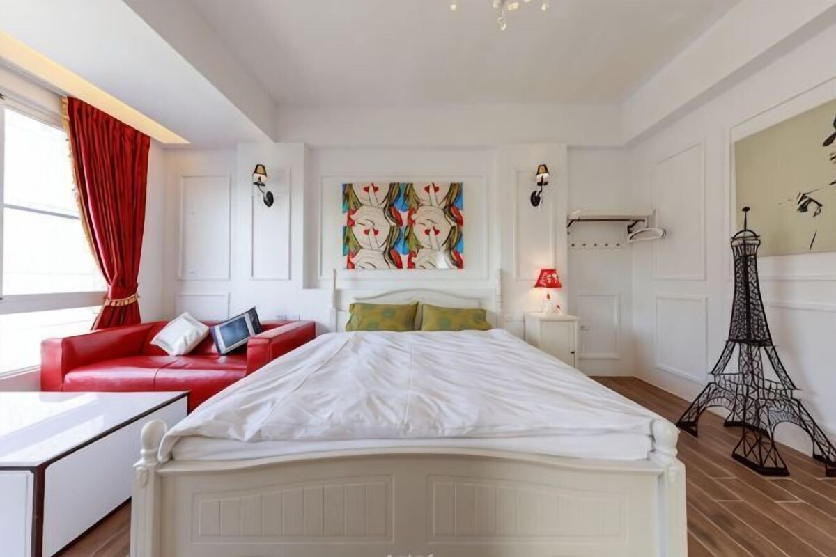 A bedroom with a white bed, red sofa, and a painting on the wall.