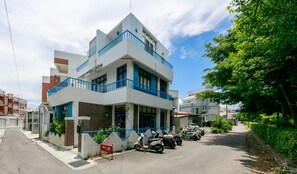A modern two-story building with a white facade and blue accents, featuring a gated entrance and parked scooters. - Oia Cafe B&B (Taitung)