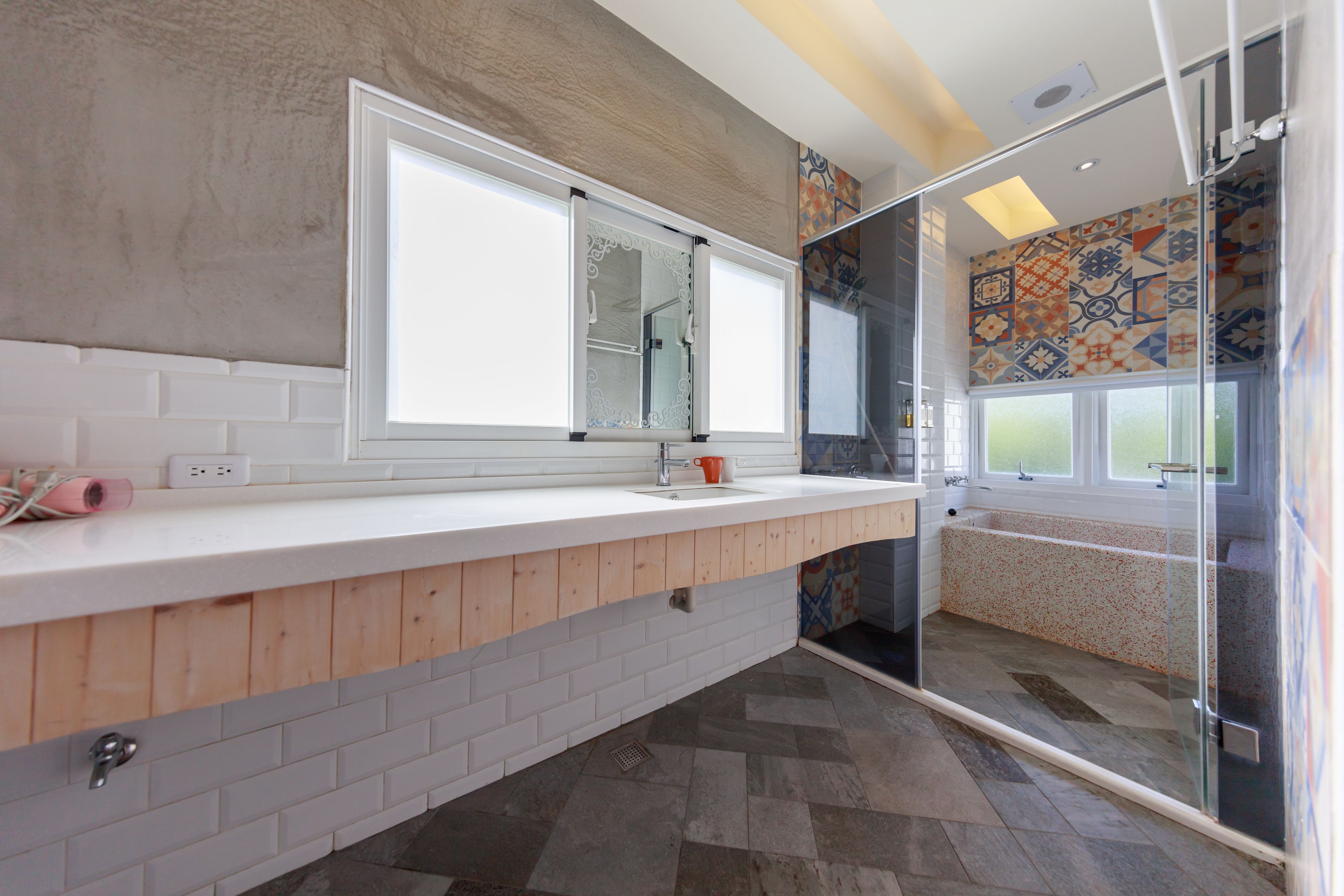 A modern bathroom with a white countertop, wooden paneling, a large mirror, a shower enclosure, and patterned tiles on the walls.