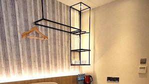 Une chambre d’hôtel moderne avec un grand canapé beige, une petite table avec une chaise, un luminaire suspendu et un mur d’accent en bois.