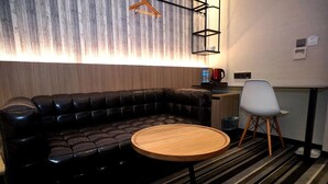 Une pièce moderne avec un canapé en cuir, une table ronde en bois, une chaise blanche et un coin cuisine équipé d’une machine à café.