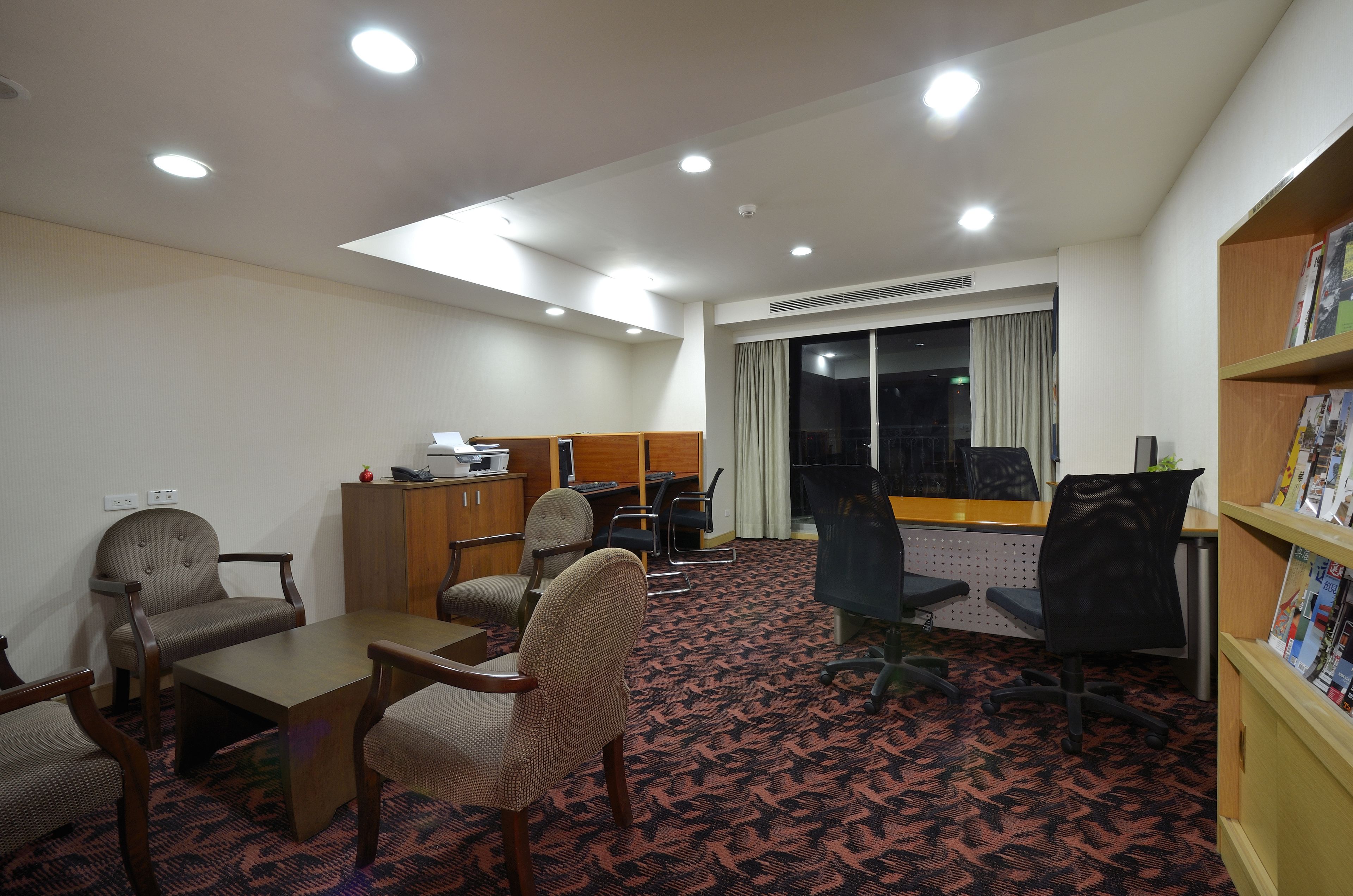 Una habitación de hotel con un ventanal grande, un escritorio, una estantería y suelo alfombrado.