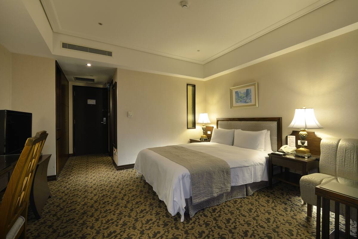 A hotel room with a large bed, two bedside tables with lamps, a chair, a desk, and a television.