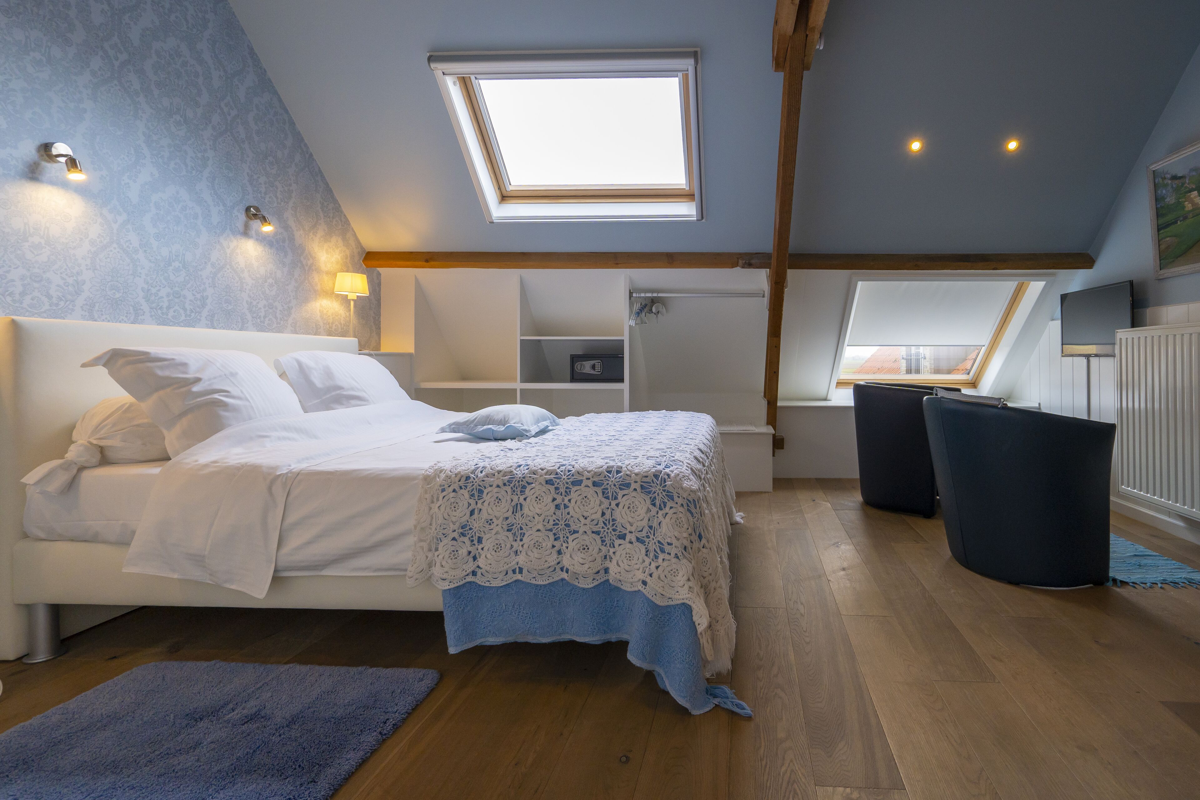 A bedroom with a skylight, a bed with white linens, a blue throw blanket, and a wooden floor.