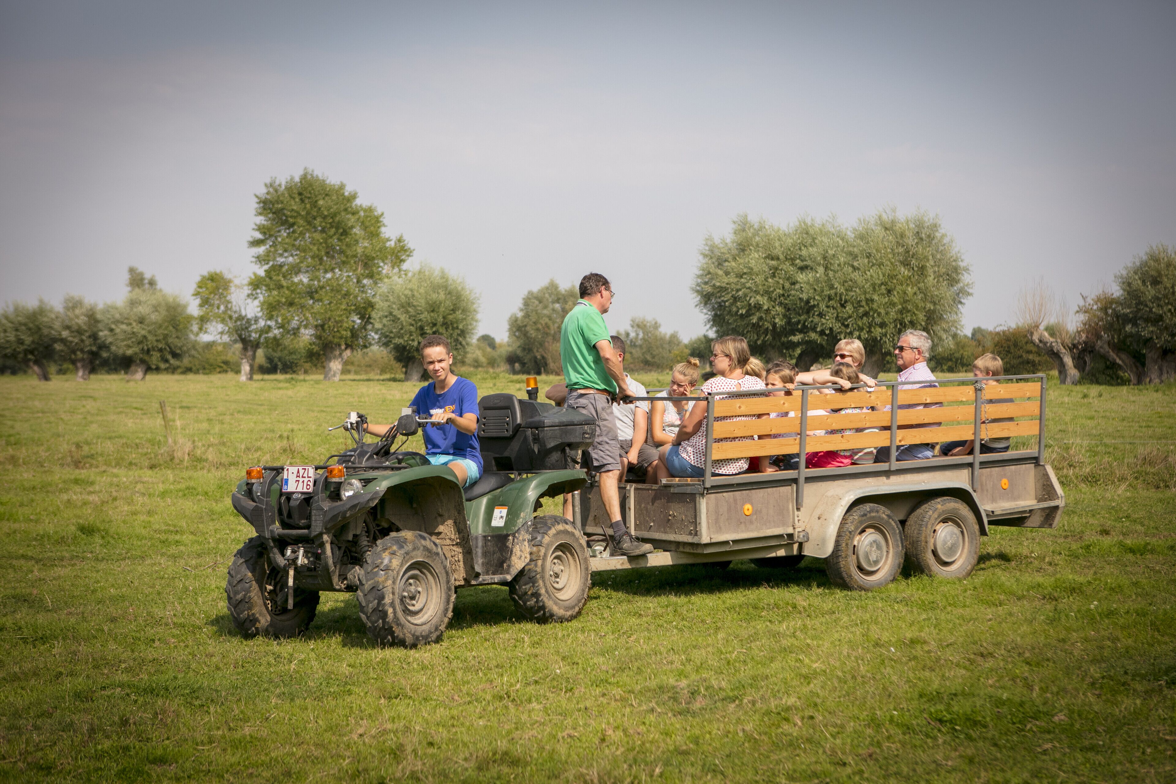 A group of people on a green ATV with a trailer in a grassy field.