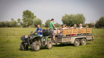 A group of people on a green ATV with a trailer in a grassy field.